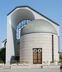 L'ingresso pirncipale, a sinistra del quale di nota di scorcio un'altra abside: quest'ultima ospita il battistero. Nella pianta (sotto) si apprezza la disposizine dei poli liturgici nell'architettura poliabsidata.